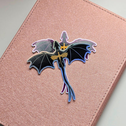 May include: A holographic dragon sticker with black wings and a gold chest, on a pink background. The dragon is depicted in flight, with a long tail. The sticker has an iridescent, shiny finish.