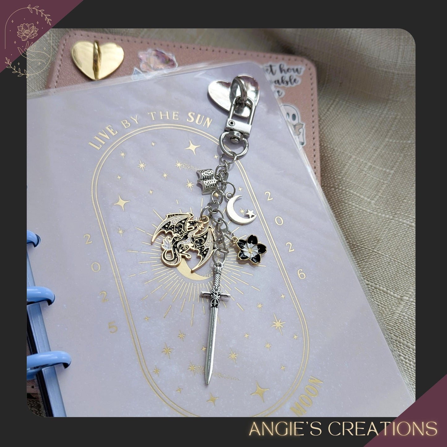 A handmade romantasy-themed Kindle charm chain featuring a detailed dragon charm, silver sword, crescent moon, flower charm, and tiny open book, attached to a silver lobster clasp. Perfect for fantasy readers and bookish accessory lovers.