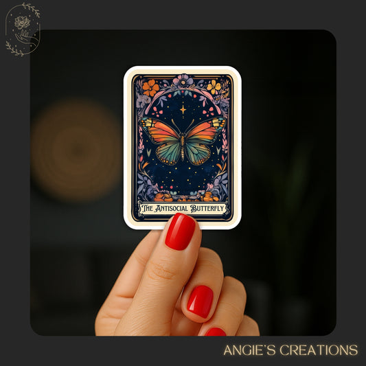 A hand holding a sticker with a colorful butterfly design against a dark background.