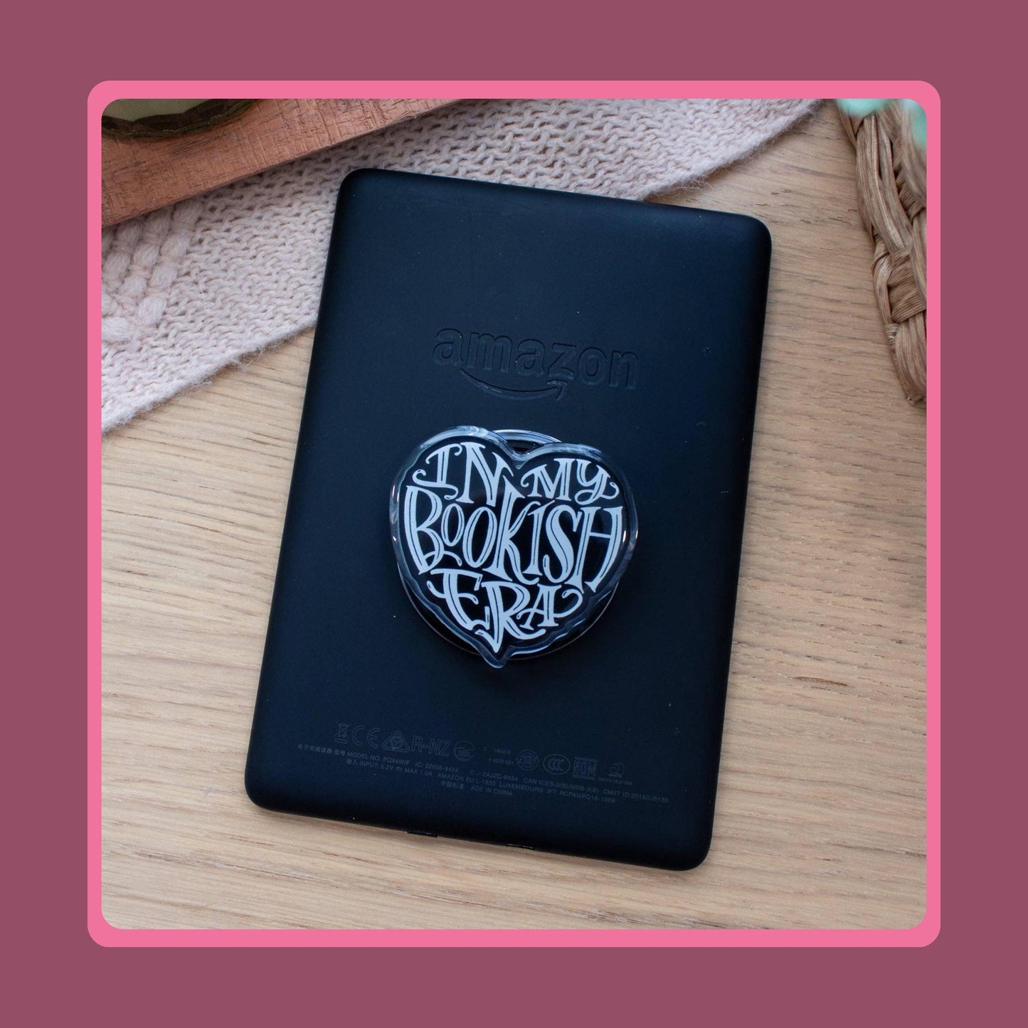 Black heart-shaped acrylic charm with white "In My Bookish Era" script lettering, sold as a matching Kindle grip and phone dust plug set.