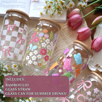 Three 16oz Libbey can glass cups with bamboo lids styled with pink tulips and daisies featuring coquette checkerboard bows, happy spring garden butterflies and florals, and rainbow gummy bear wrap designs. Each cup includes bamboo lid and glass straw, designed and finished by hand in Ottawa Canada by Angie's Creations.