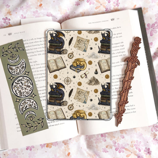 Cream Kindle insert pattern with a gold sleeping dragon and a dark dragon perched on stacked books, alongside a treasure map, compass, quill, ink well, and wax seals.