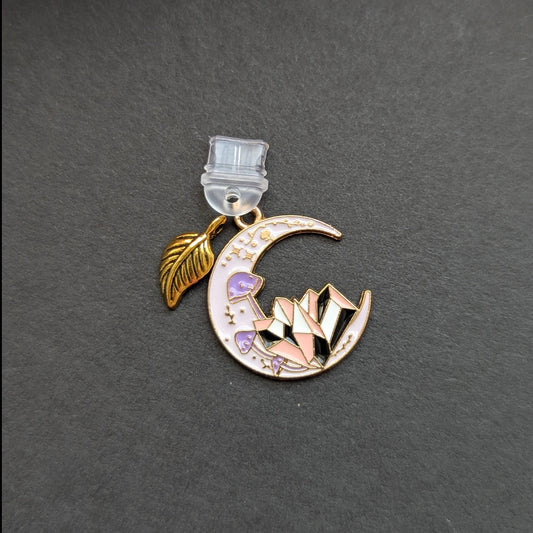 Angie's Creations hand-assembled USB-C dust plug featuring a gold crescent moon enamel charm with purple mushroom and pink geometric crystal detail paired with a gold feather leaf accent charm. Celestial cottagecore romantasy inspired phone or Kindle accessory handcrafted in Ottawa Canada.