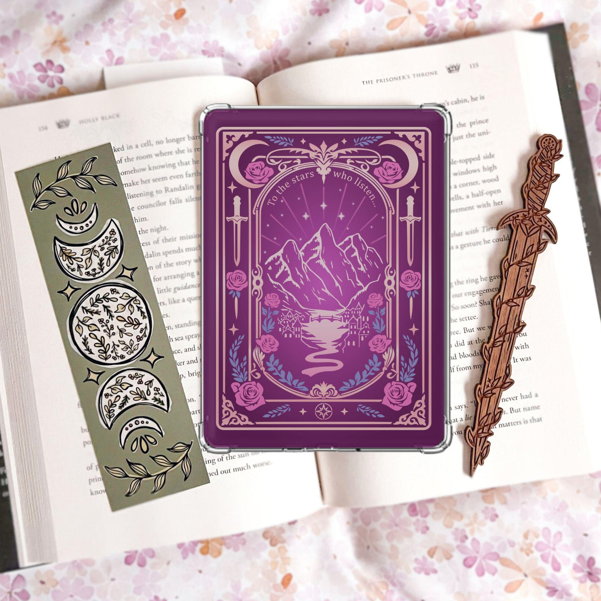 Handmade purple Kindle insert with tarot card style border, mountain landscape, roses and swords, reading "To the stars who listen," displayed on an open Holly Black book