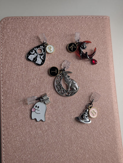 May include: Five metal charms with clear plastic attachments. One is a black planchette with white cats, one a red crescent moon with a cat and letter K, one a silver wolf on a moon with letter T, one a white ghost, and one a hat with letter B.