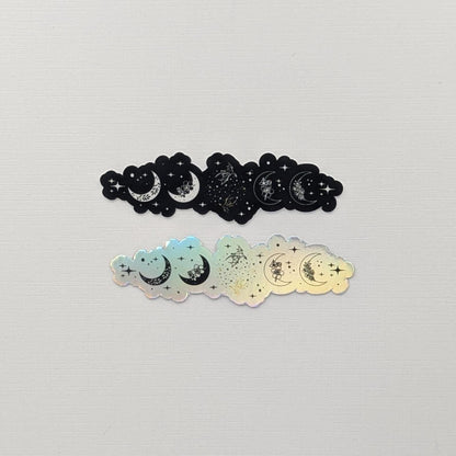 May include: Two stickers with a celestial design. One is black, the other is iridescent. Each sticker has a cloud shape with crescent moons, stars, and floral details. Ideal for crafting and DIY projects, these stickers add a touch of magic.