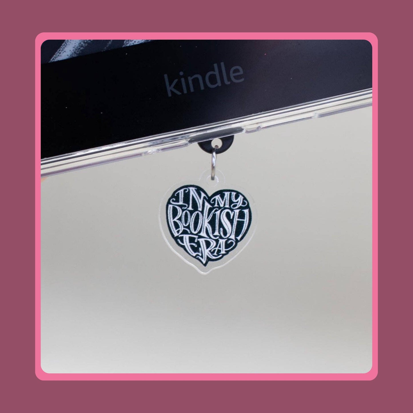 Black heart-shaped acrylic charm with white "In My Bookish Era" script lettering, sold as a matching Kindle grip and phone dust plug set.