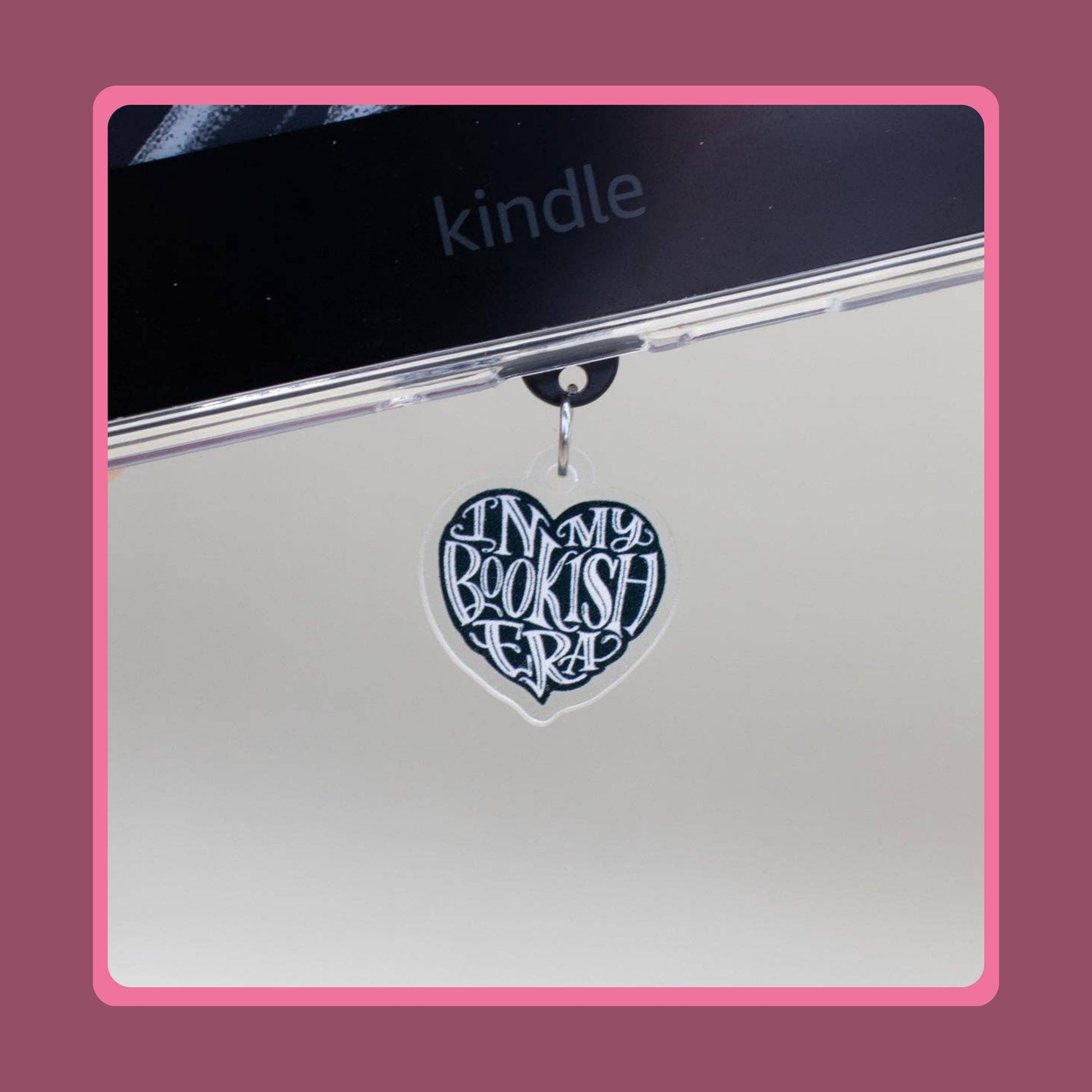 Black heart-shaped acrylic charm with white "In My Bookish Era" script lettering, sold as a matching Kindle grip and phone dust plug set.