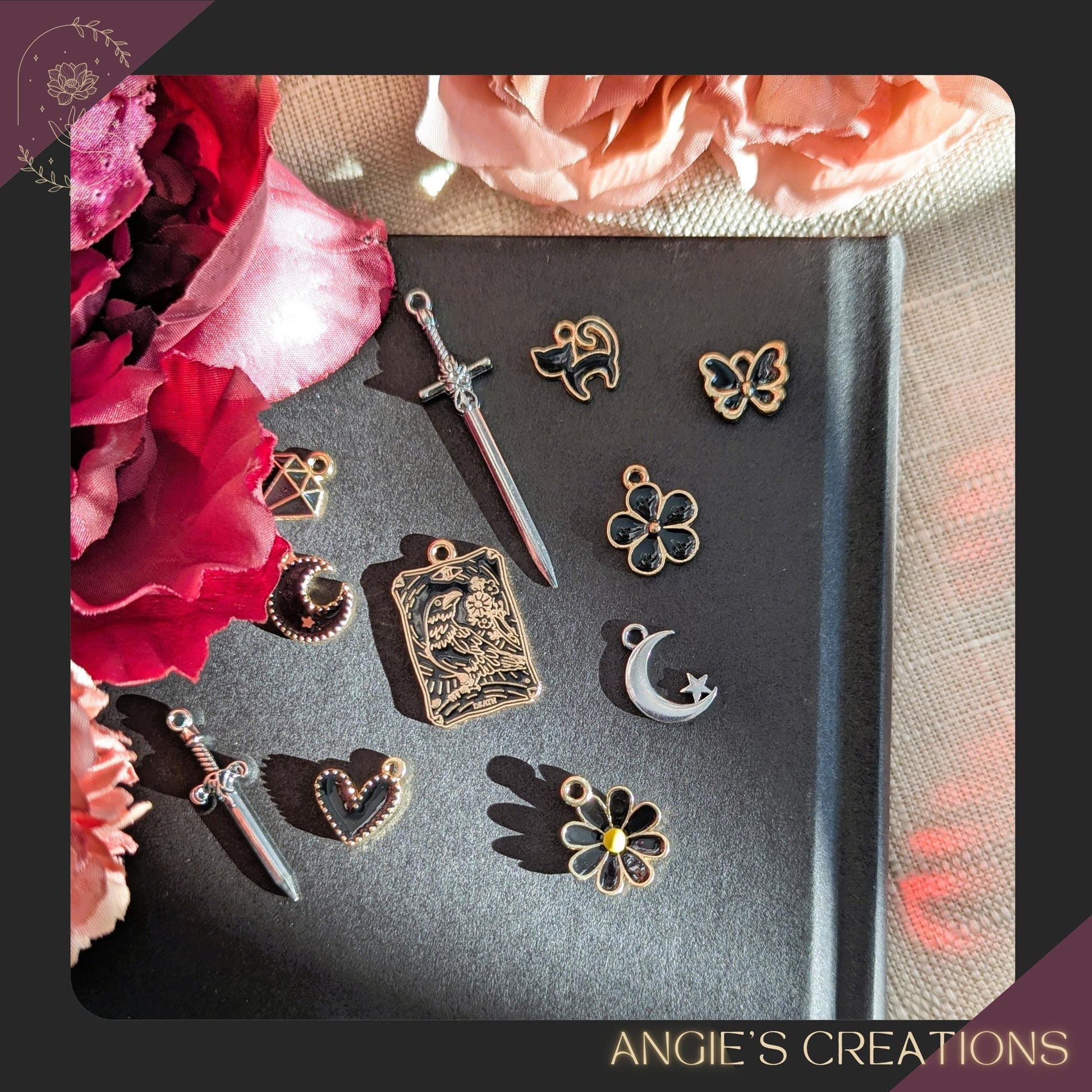 Collection of decorative charms on a dark surface with pink flowers on the side, featuring 'Angie's Creations' branding.