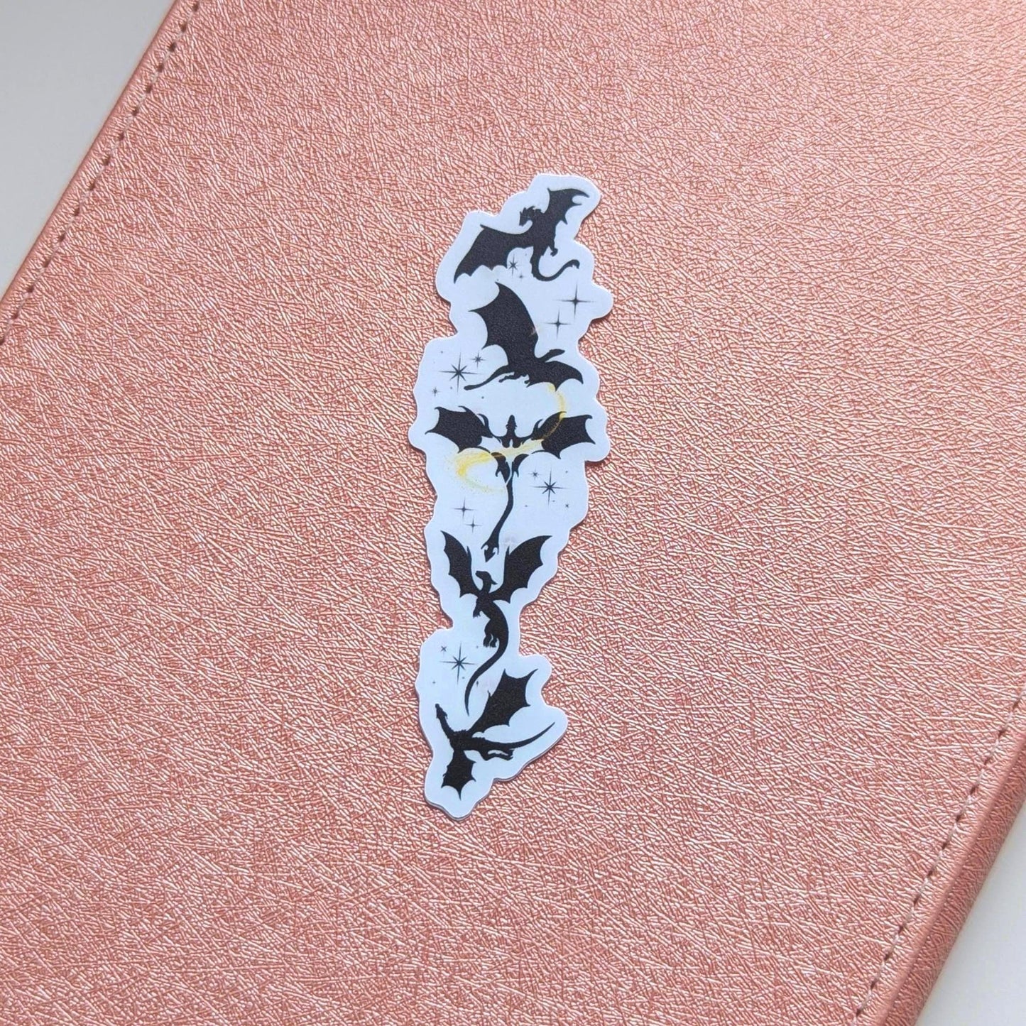 Black silhouette sticker featuring a vertical arrangement of dragons in flight, with small gold star accents, designed for Kindle or journal placement.