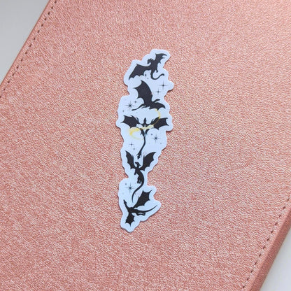 Black silhouette sticker featuring a vertical arrangement of dragons in flight, with small gold star accents, designed for Kindle or journal placement.