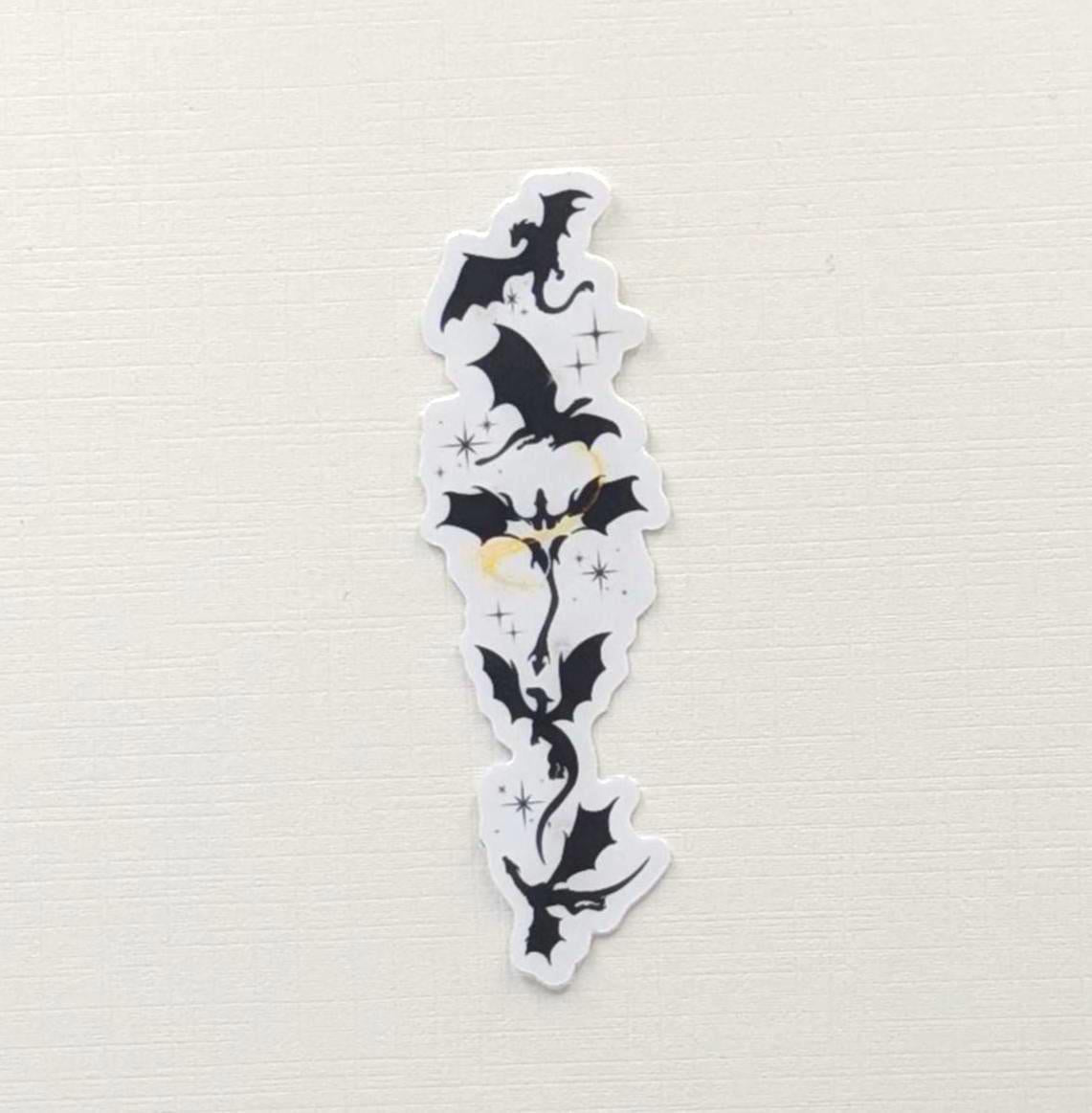 Black silhouette sticker featuring a vertical arrangement of dragons in flight, with small gold star accents, designed for Kindle or journal placement.