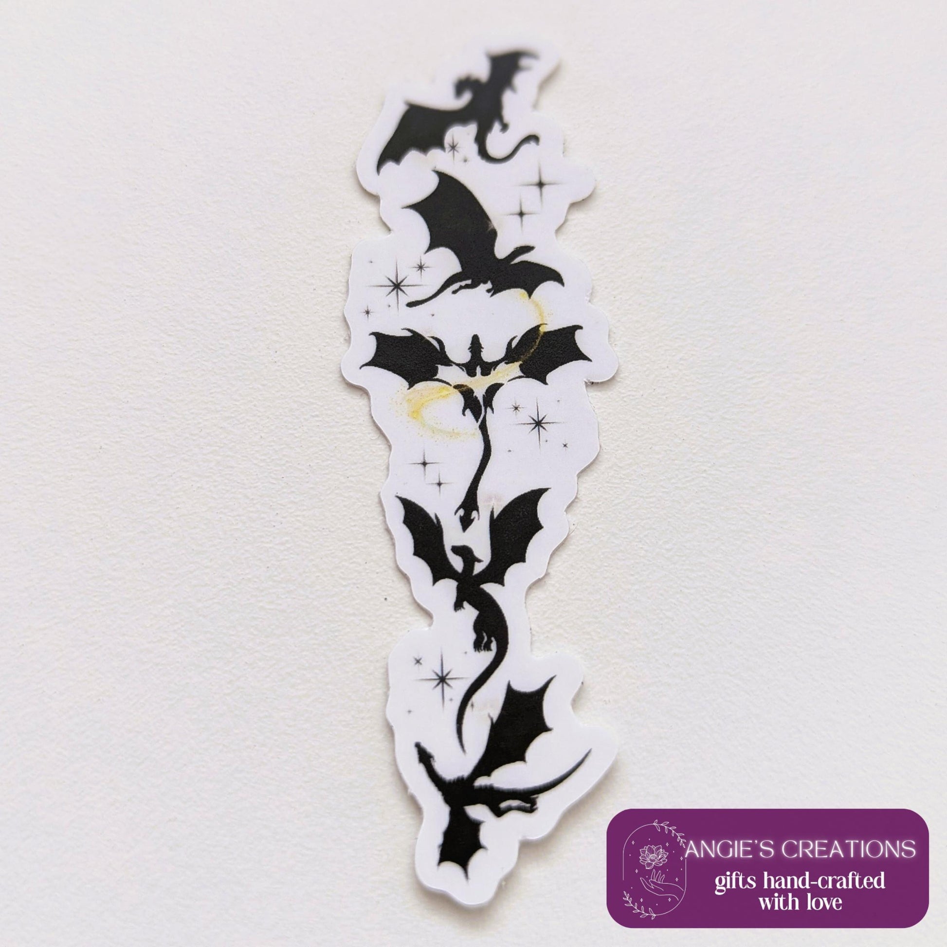 Black silhouette sticker featuring a vertical arrangement of dragons in flight, with small gold star accents, designed for Kindle or journal placement.