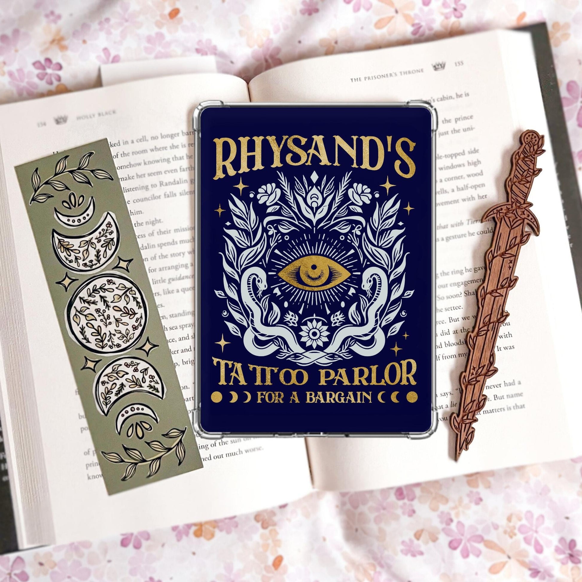 Navy and gold Kindle insert designed like a tattoo parlor sign with an all-seeing eye, twin snakes, florals, and the text "Rhysand's Tattoo Parlor, for a bargain."