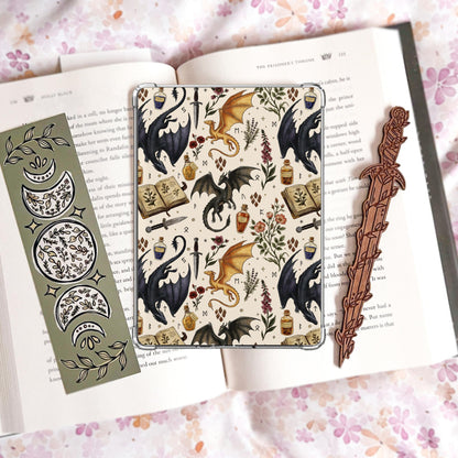 Handmade navy blue Kindle insert featuring hand drawn black and gold dragons, potion bottles, an open spell book and wildflowers in a repeating pattern, displayed on an kindle