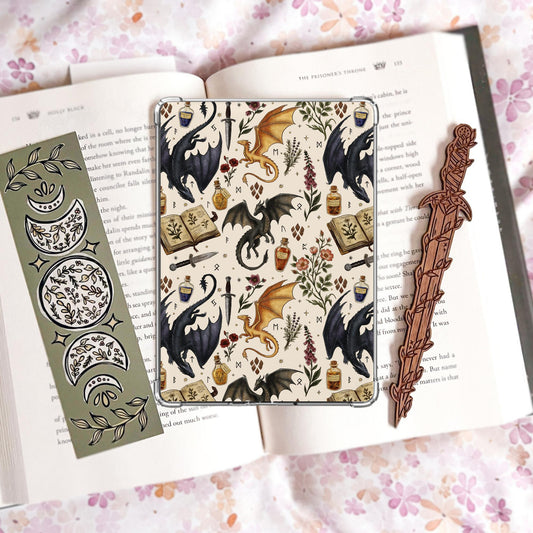 Handmade navy blue Kindle insert featuring hand drawn black and gold dragons, potion bottles, an open spell book and wildflowers in a repeating pattern, displayed on an kindle