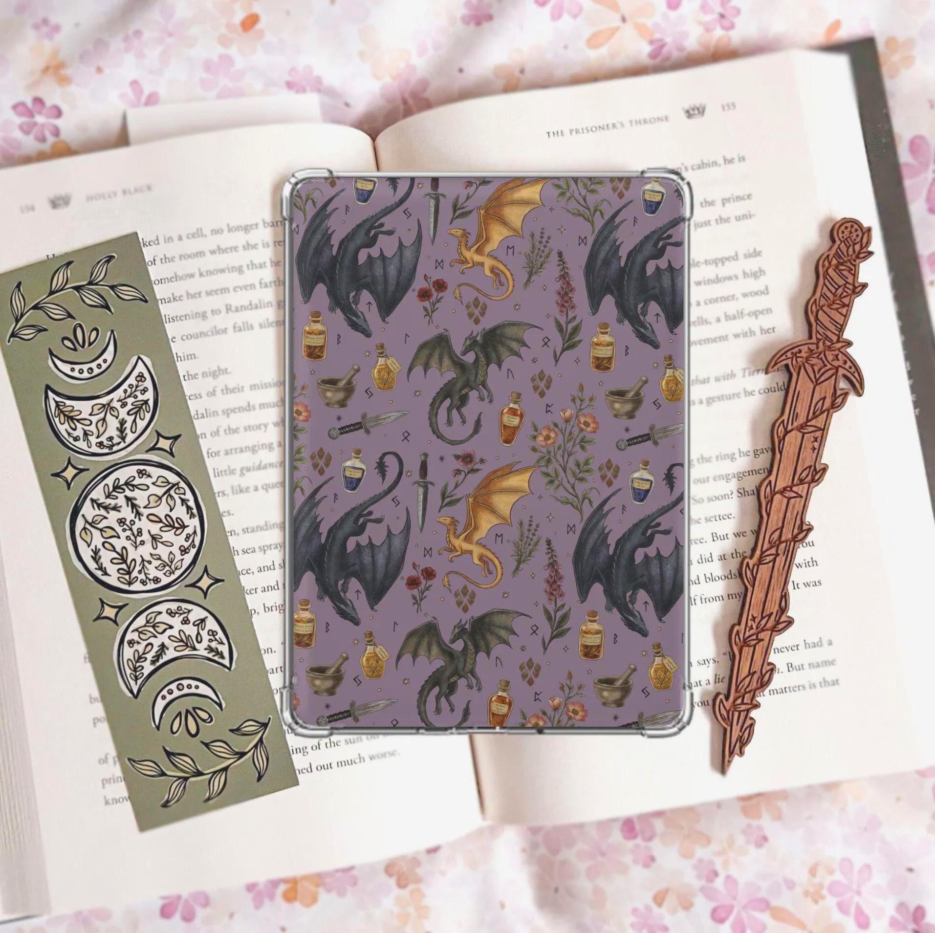Handmade navy blue Kindle insert featuring hand drawn black and gold dragons, potion bottles, an open spell book and wildflowers in a repeating pattern, displayed on an kindle