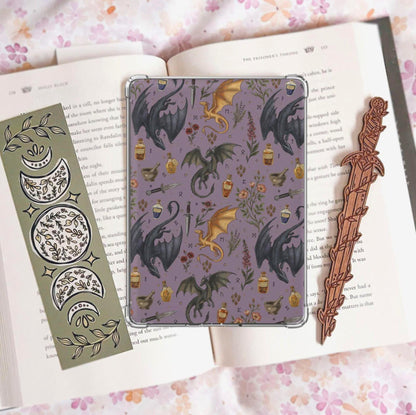 Handmade navy blue Kindle insert featuring hand drawn black and gold dragons, potion bottles, an open spell book and wildflowers in a repeating pattern, displayed on an kindle